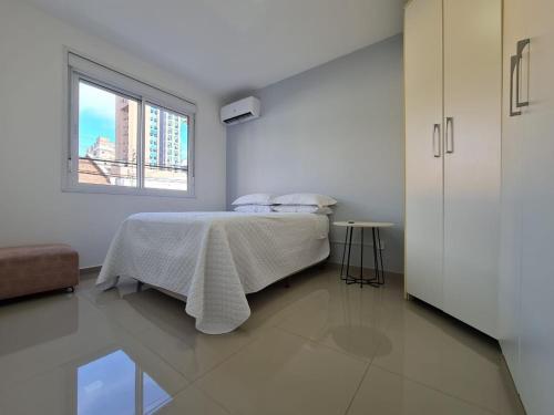 - une chambre blanche avec un lit et une fenêtre dans l'établissement Belo Apartamento Eldorado II Master Collection, à Passo Fundo