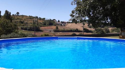 a large blue swimming pool with a hill in the background at Quintal do Freixo - Country House in Sobral de Monte Agraço