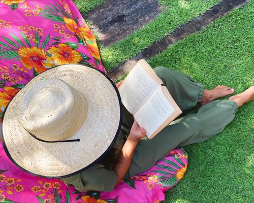 a person sitting on the grass with a hat and a book at Paracuru Kitefriends Lux Pousada in Paracuru