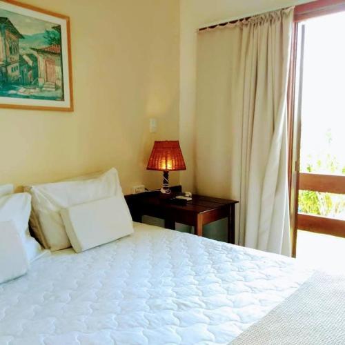 a bedroom with a white bed and a desk with a lamp at Pousada Guaratiba in Prado