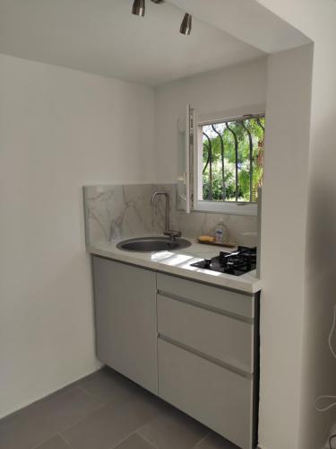 une cuisine blanche avec un évier et une fenêtre dans l'établissement Magnifique Rez de Jardin Tropézien, à Saint-Tropez