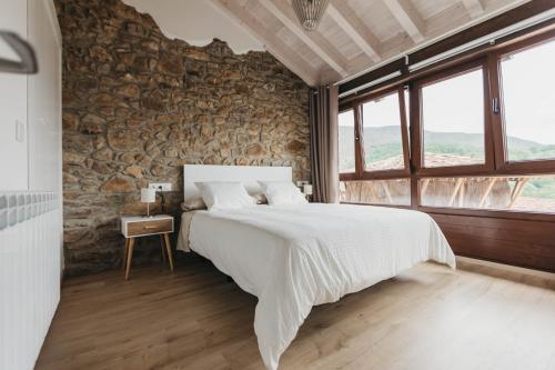 um quarto com uma cama grande e uma parede de pedra em EL CORRAL DEL CARTERU - Casa Rosales em Infiesto