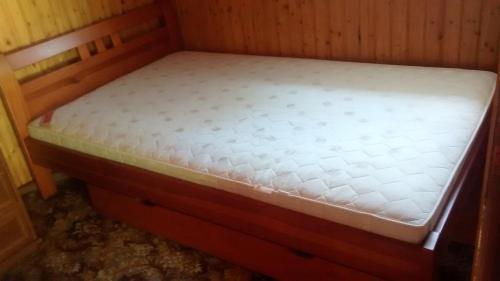 a bed in a wooden room with a white mattress at dom letni in Stare Jabłonki