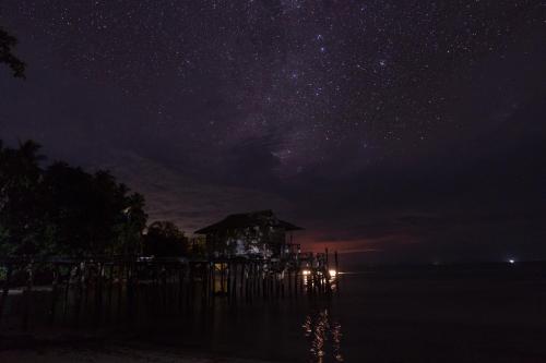 a starry night with a house on the water at Alter Native Stay in Tapokreng