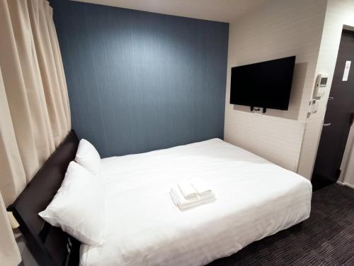 a bedroom with a white bed with a flat screen tv at GLOU Higashi Shinjuku in Tokyo