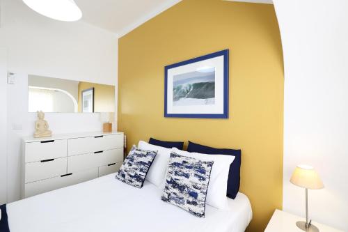 a bedroom with a white bed and a yellow wall at Big Wave Apartment in Nazaré