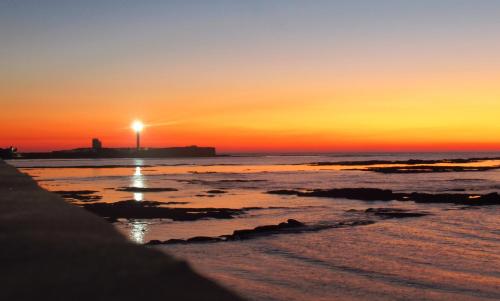 a sunset on the beach with a lighthouse in the background at Oceanum Visum Spa Deluxe in El Trocadero