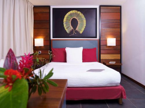 una habitación de hotel con una cama con almohadas rojas y aumed en Hotel Mercure Kourou Ariatel, en Kourou
