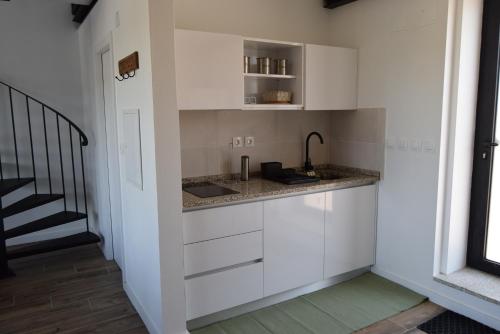a kitchen with white cabinets and a sink and a staircase at Casa do Chão do Cruzeiro in Arcozelo
