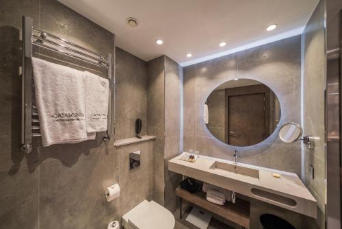 a bathroom with a toilet, sink, mirror and bath tub at Catalonia Gran Vía Bilbao in Bilbao