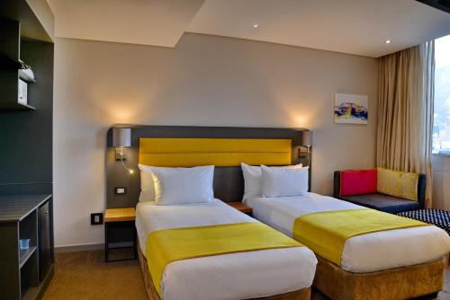 a hotel room with two beds and a chair at Cresta Grande Cape Town in Cape Town