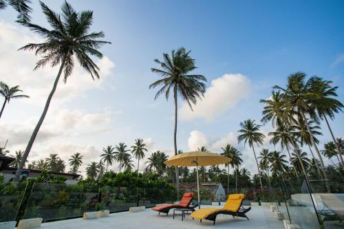 three chairs and an umbrella in front of palm trees at Sielen Diva in Unawatuna