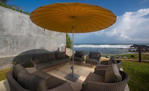 a patio with couches and an umbrella and the ocean at Sielen Diva in Unawatuna