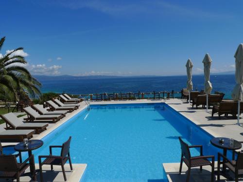 a swimming pool with chairs and tables and the ocean at Barbagiannis House in Ormos Panagias