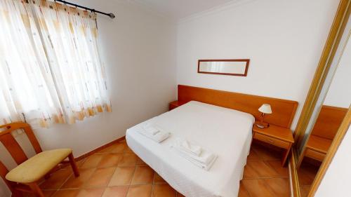 a small bedroom with a white bed and a chair at Monte dos Avós Village - Pet Friendly in Tavira
