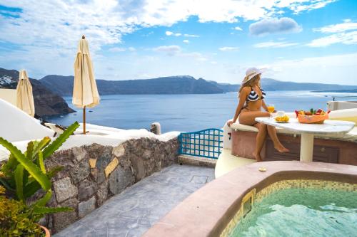 a woman sitting at a table next to a swimming pool at Santorini Paradise Cave Houses in Oia