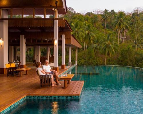 two people sitting on a deck next to a swimming pool at Symphony Samudra Beachside Jungle Resort And Spa in Port Blair