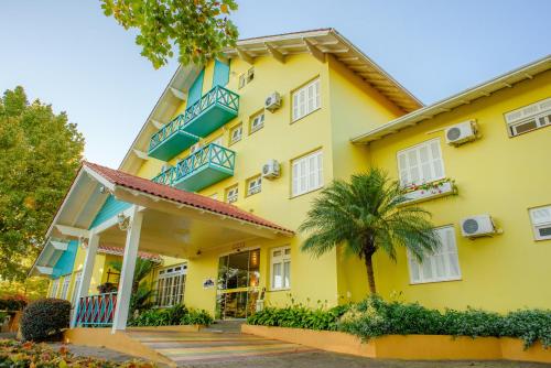 a yellow house with blue balconies and a palm tree at Hotel Pousada da Neve in Nova Petrópolis