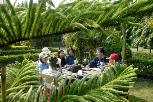 a group of people sitting around a table in a garden at Jungle Safari Resort in Sauraha