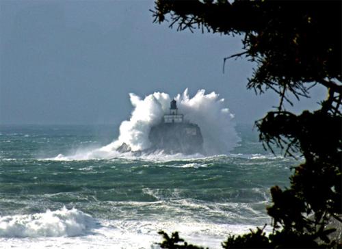 a lighthouse in the ocean with a large wave at Webb's Scenic Surf in Cannon Beach
