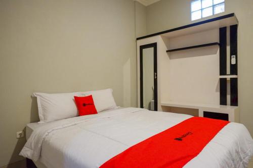 Un dormitorio con una almohada roja en una cama blanca en RedDoorz Plus near Jogja City Mall 5, en Yogyakarta