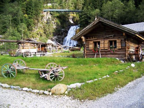 a log cabin with a wagon in front of a waterfall at Alfaierhof-Bergheimat in Gschnitz