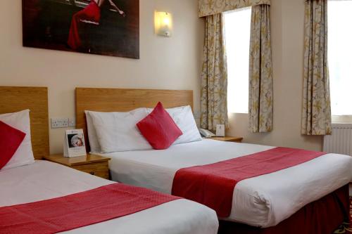 two beds in a hotel room with red pillows at Best Western Greater London in Ilford