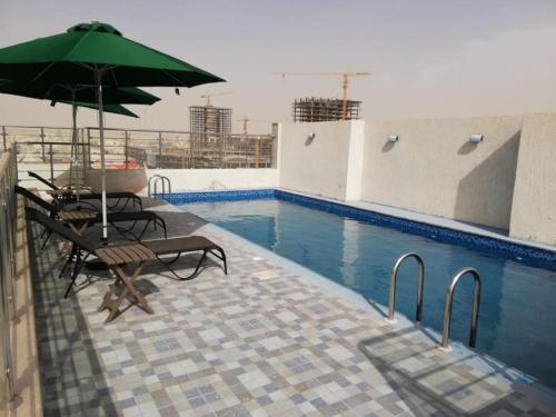 una piscina con ombrellone e sedie verdi di Ruve Jeddah Hotel a Gedda