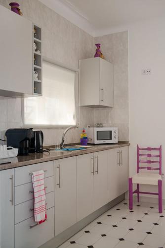 a kitchen with white cabinets and a microwave and a chair at Alojamento das Fontes in Alenquer