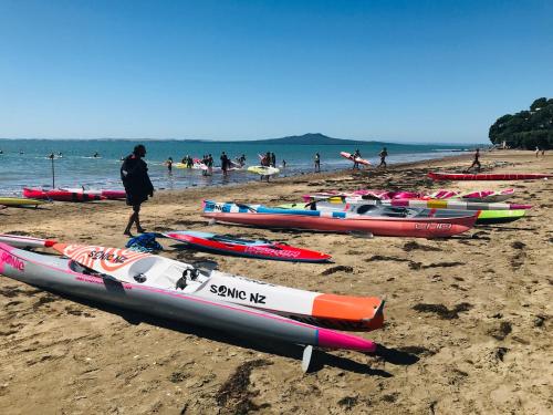 a group of kayaks on a beach with people in the water at Whitby Studio - Mairangi Bay Beach in Auckland
