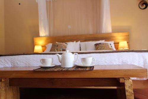 a bed with a table with two cups on it at Kisubi Forest Cottages in Entebbe