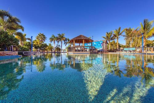 a large swimming pool with palm trees and a gazebo at Ningaloo Caravan and Holiday Resort in Exmouth