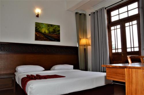 a bedroom with a bed and a desk and windows at Heaven Seven Nuwara Eliya in Nuwara Eliya