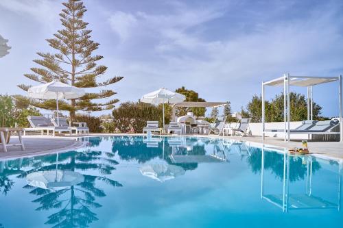 una piscina con agua azul, sillas blancas y un árbol en La Maison Private Villa, en Agia Paraskevi