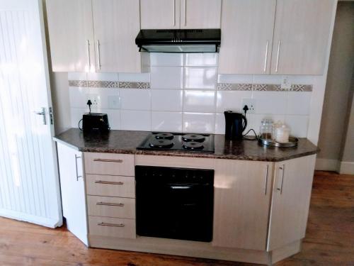 a kitchen with white cabinets and a black stove top oven at Cozy Cottage Van Reenen in Van Reenen