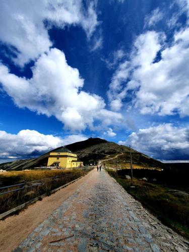 a person walking down a dirt road under a cloudy sky at Hotel Rezydencja AS & Spa-Najwyżej w Karpaczu in Karpacz