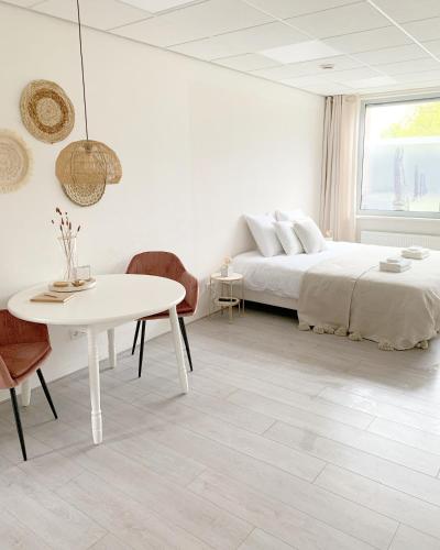 a white bedroom with a bed and a table at Sea you soon in Den Burg