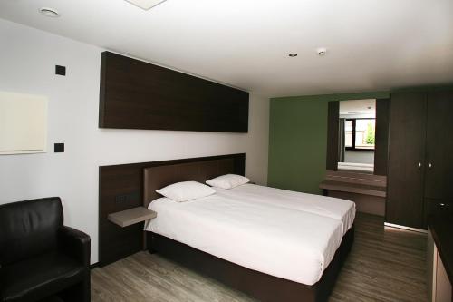 a bedroom with a white bed and a black chair at Hotel Au Prince Royal in Leopoldsburg