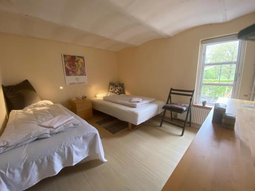 a bedroom with two beds and a chair and a window at Margretelyst Ferielejlighed in Farsø