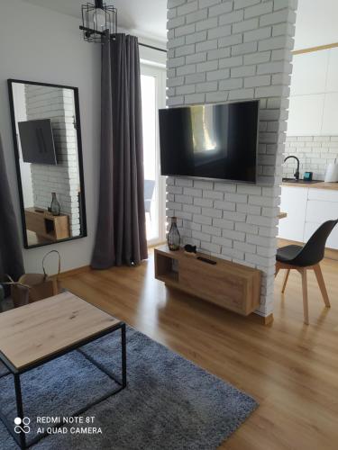 sala de estar con TV en una pared de ladrillo blanco en Apartament dla Dwojga, en Dziwnówek