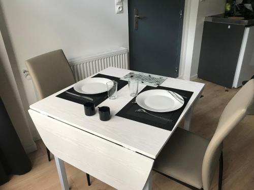 a white table with two plates and glasses on it at Appartements du Vally - Guingamp in Guingamp