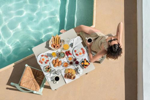 a woman sitting at a table with food next to a pool at Argo Boutique Hotel in Naxos Chora