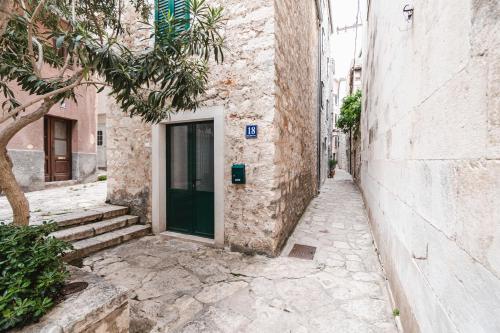 an alley with a green door in a stone building at Amoretta rooms in Šibenik