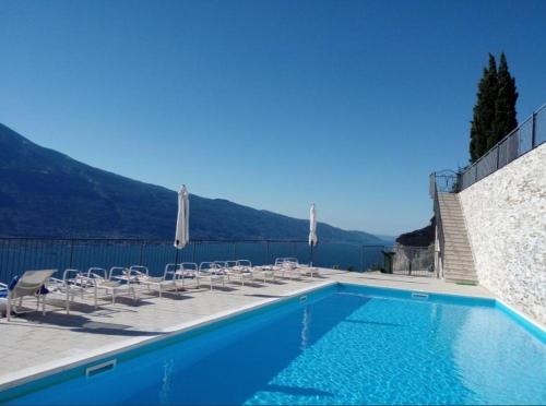 a blue swimming pool with chairs and a view of the water at Appartamento Flora in Tremosine Sul Garda