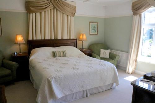 a bedroom with a bed and two chairs and a window at Stoneborough House B&B in Budleigh Salterton