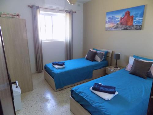 een slaapkamer met 2 bedden met blauwe lakens en een raam bij Sunshine Holiday Apartment 5 with Spectacular Seaviews in St Paul's Bay