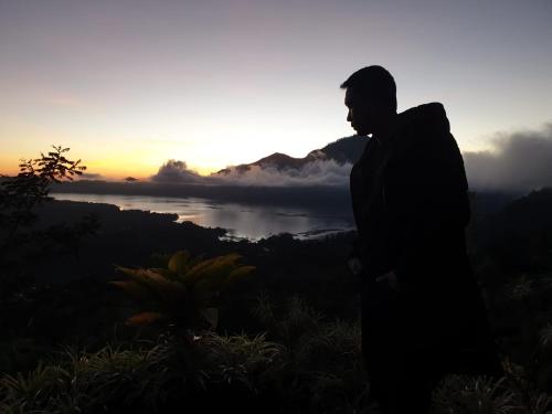 a man standing on top of a hill with a sunset at Tukadsari camping in Kintamani