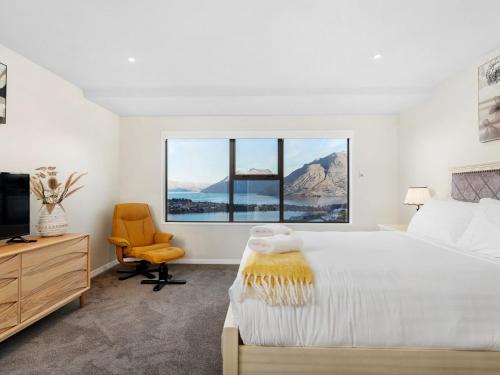a white bedroom with a large bed and a chair at Classy Conifer by Relaxaway Holiday Homes in Queenstown