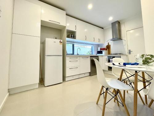 a white kitchen with a table and a refrigerator at Brighton Villas by Readyset in Melbourne
