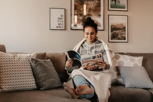 a woman sitting on a couch reading a book at Hoamat House I Boutique Apartments in Sankt Margarethen im Lungau